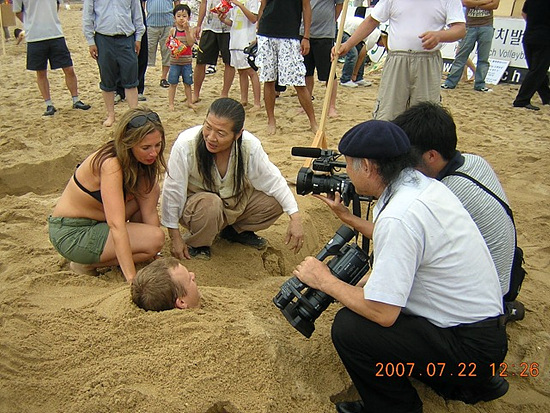 NSP통신-2007년 여름 광안리해수욕장에서 모래찜질연구회 정순근회장(가운데)이 외국인에게 모래찜질을 시연하고 있다.