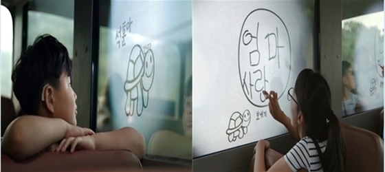 NSP통신-통학버스에 구현된 스케치북 윈도우를 바라보고 있는 어린이의 모습(좌)과 통학버스에 구현된 스케치북 윈도우 기술을 이용해 창문에 글씨를 쓰고 있는 어린이의 모습(우)