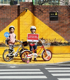 NSP통신-서울 흥인초등학교 앞 교통안전을 위해 설치된 옐로카펫에서 두 어린이가 3M 안전 반사지 스티커가 부착된 자전거를 끌며 자전거 안전의 중요성을 알리고 있다 (한국쓰리엠)