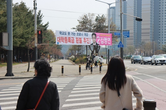 NSP통신-김명연 후보가 대학등록금 환불 추진 공약을 거리 현수막에 내걸자 지나가는 시민들이 관심 있게 지켜보고 있다. (김명연 후보 캠프)