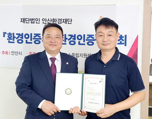 NSP통신-홍희관 안산환경재단 대표(왼쪽)가 이낙원 부흥금속공업사 대표에 환경인증 수여 후 함께 기념촬영을 하고 있다. (사진 = 안산환경재단)