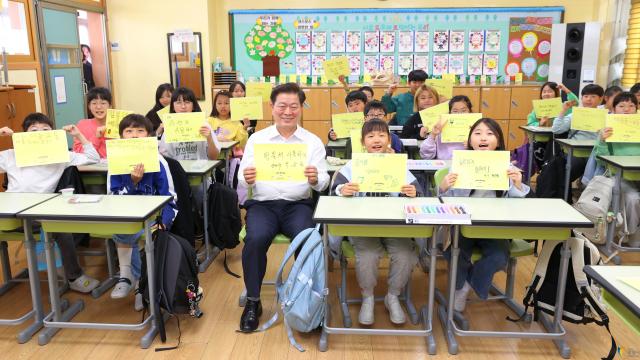 NSP통신-박승원 광명시장이 2024년 11월 광명남초등학교를 방문해 초등학생들과 광명시의 탄소중립 정책에 대해 소통하는 가운데 자신만의 탄소중립 실천 방법을 작성한 종이를 들고 기념사진을 촬영하고 있다. (사진 = 광명시)