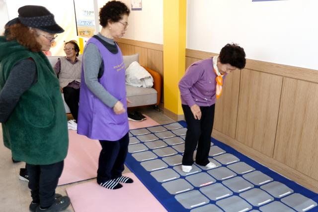 NSP통신-한 어르신이 스텝 운동 매트에서 불빛을 따라 블록을 밟고 있다. (사진 = 경기도)